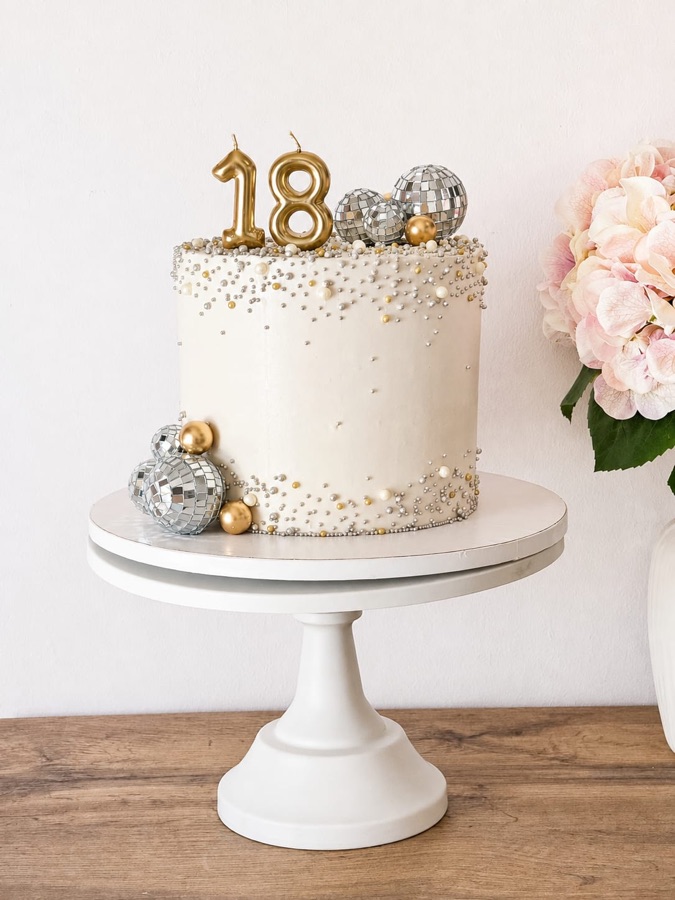 Tarta blanca con perlas plateadas, bolas de espejo y número dieciocho dorado