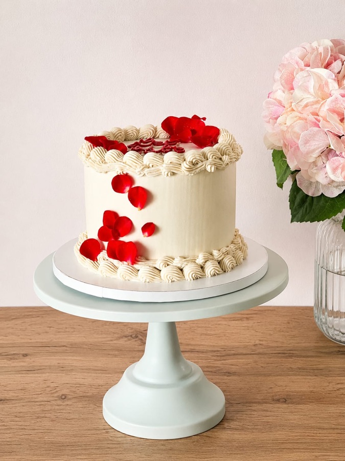 Tarta marfil con piping vintage y pétalos rojos cayendo por un lateral