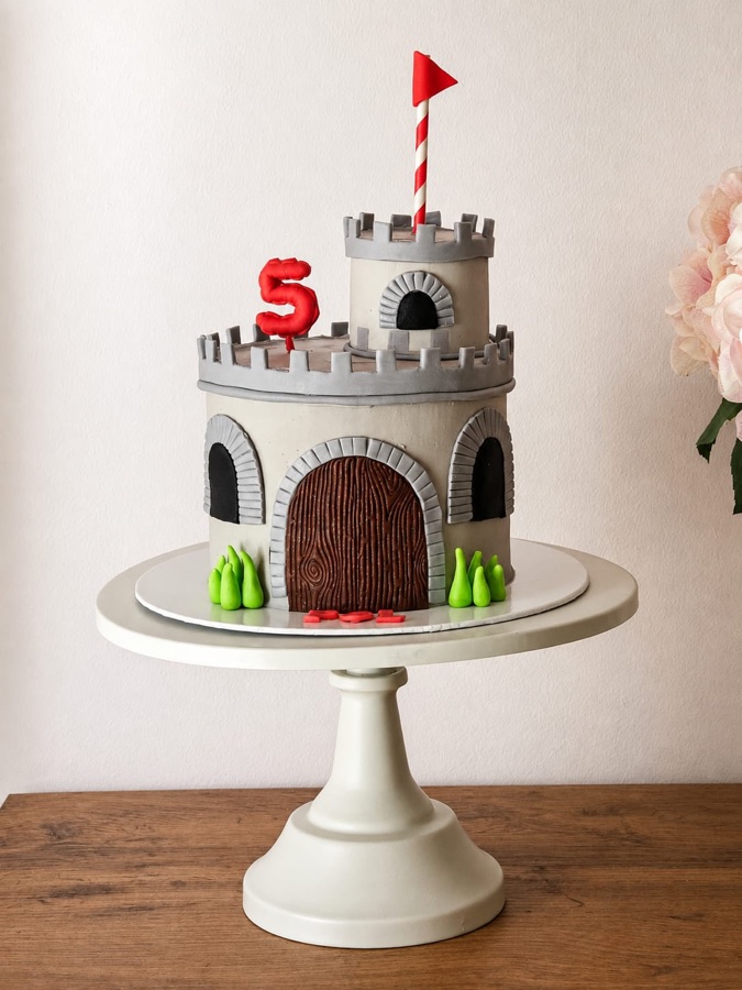 Tarta esculpida con forma de castillo de piedra gris con bandera y número cinco