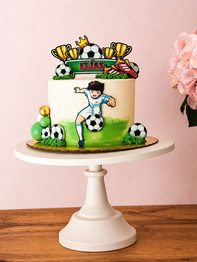 Tarta de fútbol con un futbolista modelado, césped verde, balones y trofeos