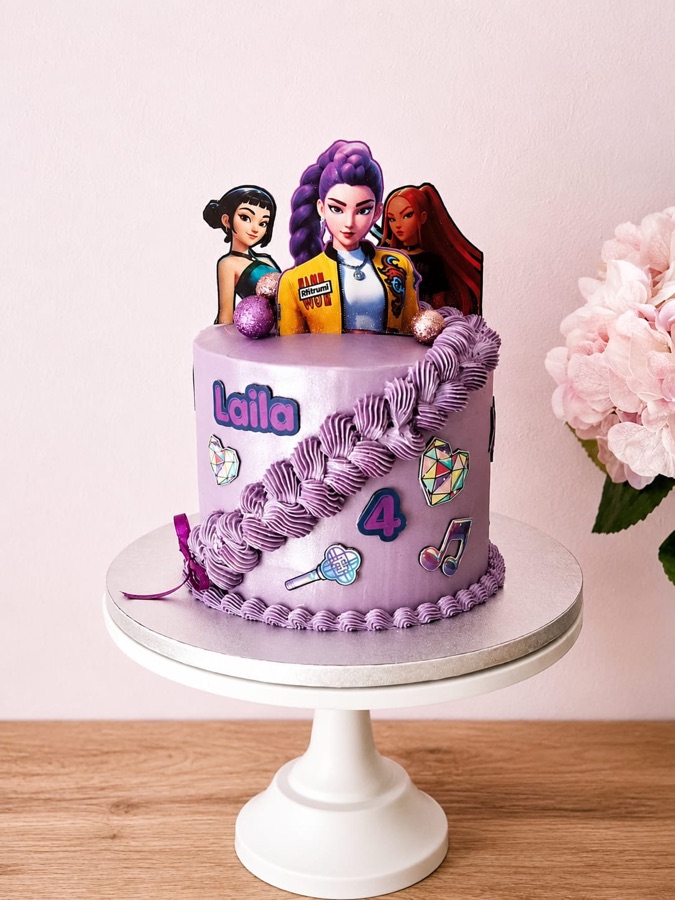 Tarta lila con volantes de crema, figuras del grupo y aplicaciones de colores