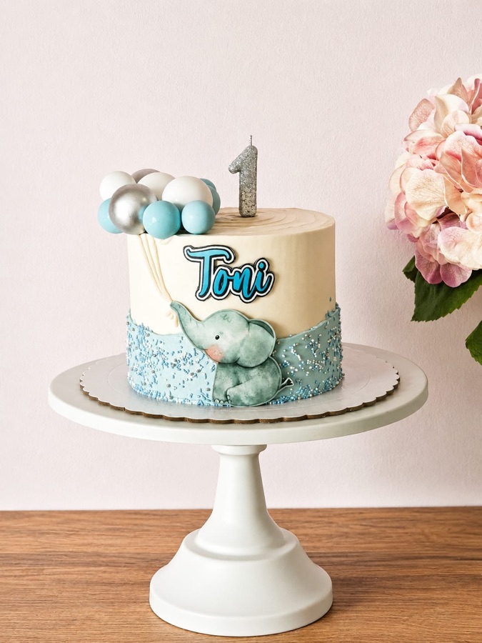 Tarta en azul claro con un elefante modelado, globos y el número uno