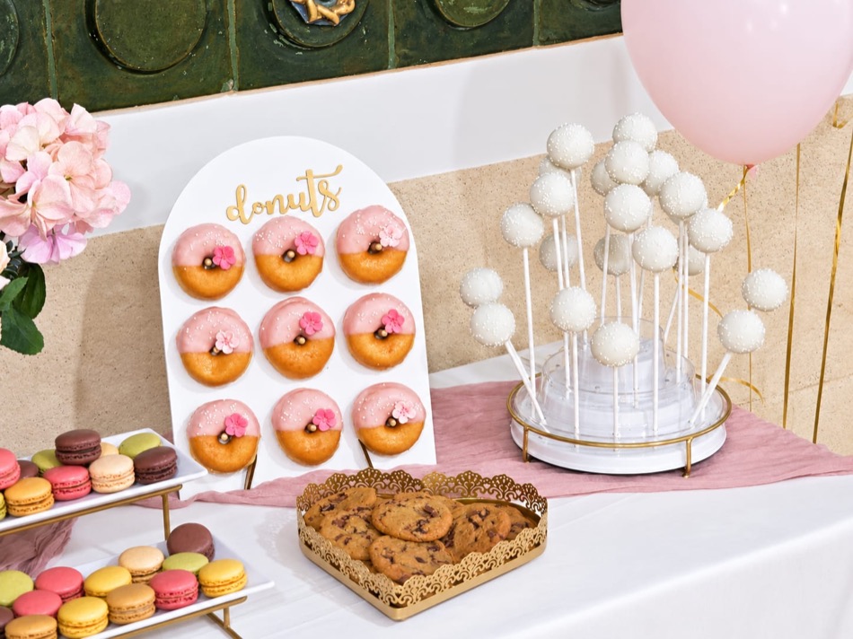 Detalle de mesa con expositor de donuts en arco, cake pops, macarons, galletas y un globo