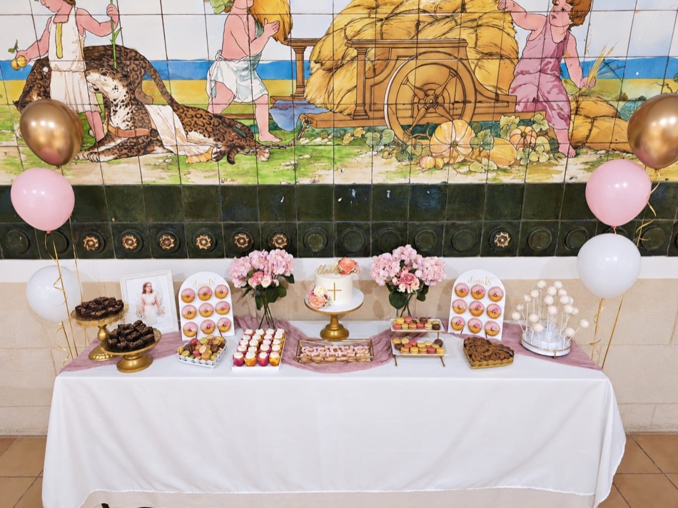 Mesa de comunión en blanco y rosa con tarta, panel de donuts, cake pops, bombones, muffins y flores