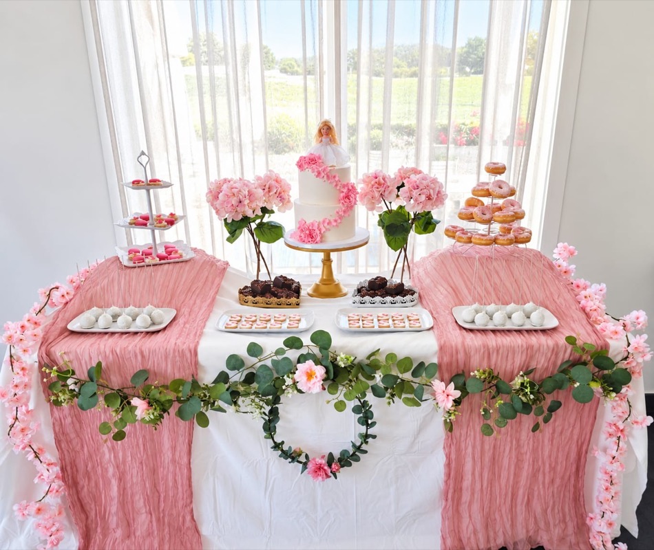 Mesa en rosa con tarta, torre de donuts, macarons, brownies, tartaletas, hortensias y guirnalda de eucalipto